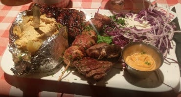 Een gemengd grillbord bij Amadeus met ribbetjes, spiesjes, een gepofte aardappel in folie, coleslaw van rode kool en een dipsausje, op een rood-wit geruit tafelkleed