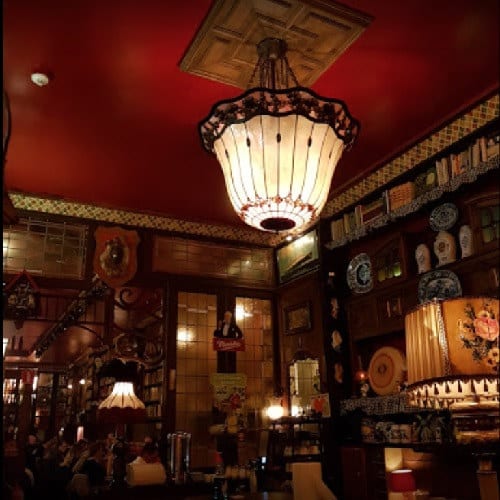 De zaal van Amadeus Antwerpen 2 met een grote glas-in-lood hanglamp en decoratieve borden aan de wand