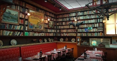 Boekenwanden vol boeken boven de rode banken en geruite tafels van Amadeus Antwerpen 2