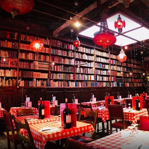 Boekenwanden tot aan het plafond en rode lantaarns boven de geruite tafels van Amadeus Brussel